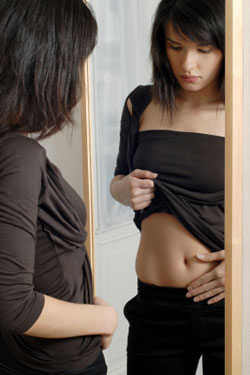 woman looking at belly in mirror