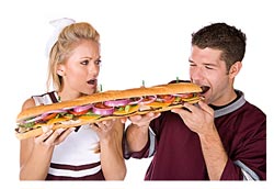 woman helping man who is eating an enormous sandwich